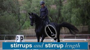 A person in riding gear is riding a black horse in an outdoor arena. The image highlights the horse’s stirrup, with the text dressage stirrup length and stirrups at the bottom.