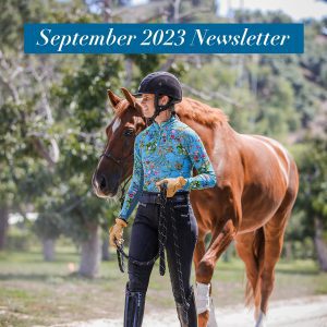 Amelia, wearing a helmet, floral shirt, gloves, and riding pants, leads a chestnut horse by its reins outdoors with trees behind her. Text reads: September News 2023 Newsletter.