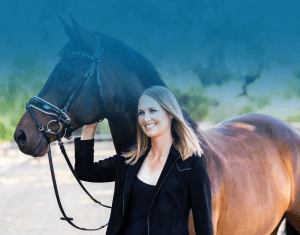 A smiling woman with straight, shoulder-length blonde hair stands next to a brown horse, holding its reins. Outdoors amidst blurred greenery and a blue gradient above, subtle patterns emerge in the scene’s natural tranquility.