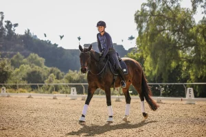 Amelia Newcomb riding a dark bay horse, she it patting them and walking with a long rein.