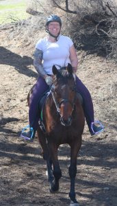 Sheena Burgos smiling while on her horse and taking them for a trail ride.