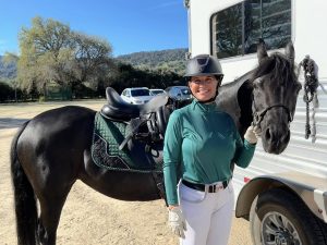 Stacie Rice smiling and posing with her horse who is tacked up and ready for a dressage show.