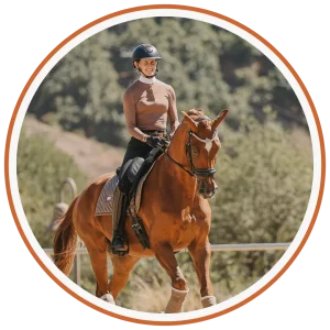 A person wearing a helmet and brown long-sleeve shirt is riding a chestnut horse outdoors, surrounded by greenery and sunlight—a perfect scene of contact and connection with nature.