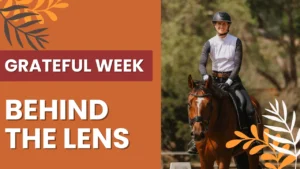 A person in riding gear smiles while sitting on a brown horse outdoors, reflecting their love of the horse. The image features the text GRATEFUL WEEK and BEHIND THE LENS on an orange background with leaf illustrations.